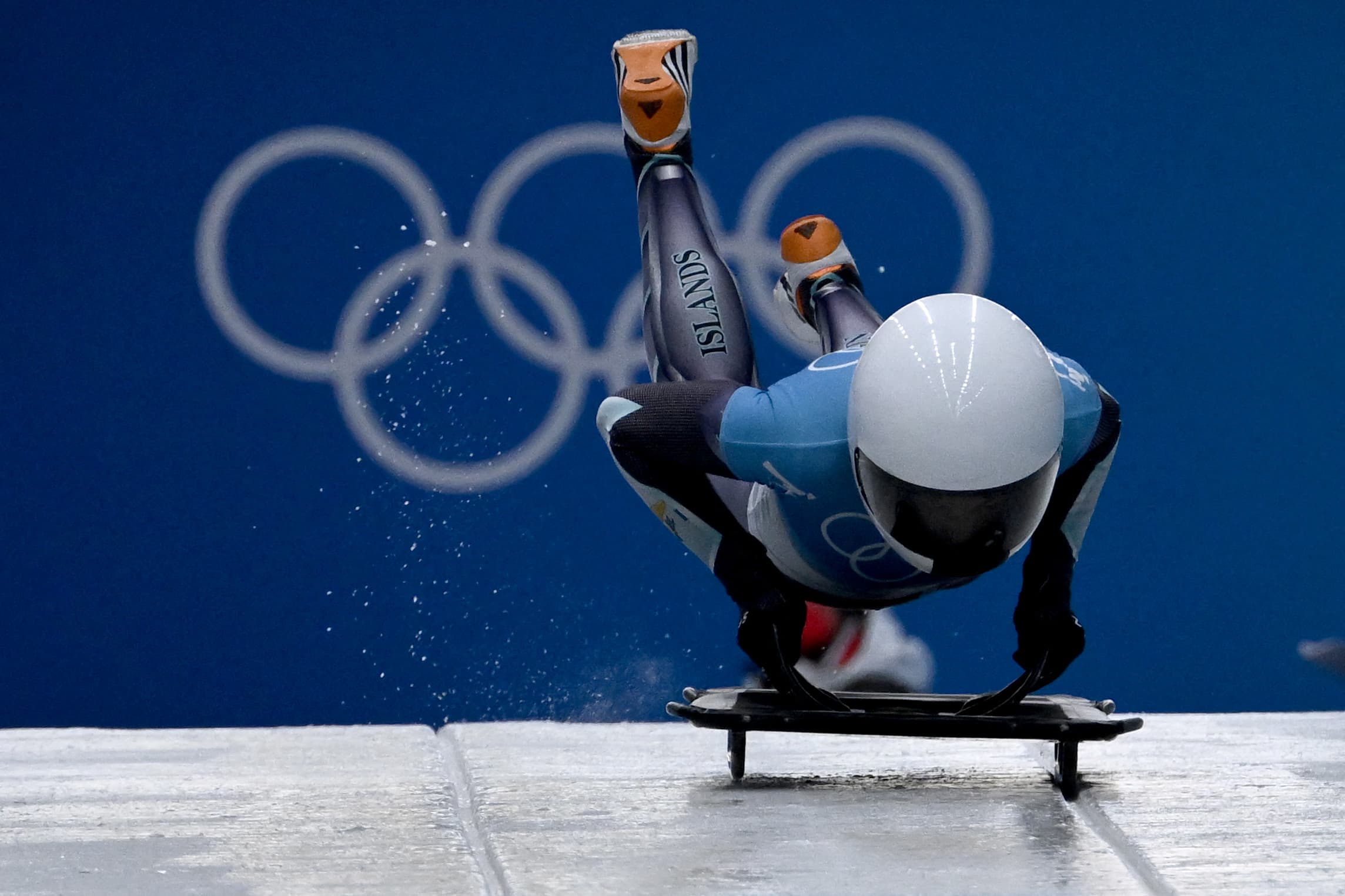 Katie Tannenbaum hopping onto a skeleton sled with the Olympics rings behind her.
