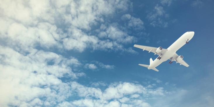 Airplane in flight with blue sky and clouds in background.